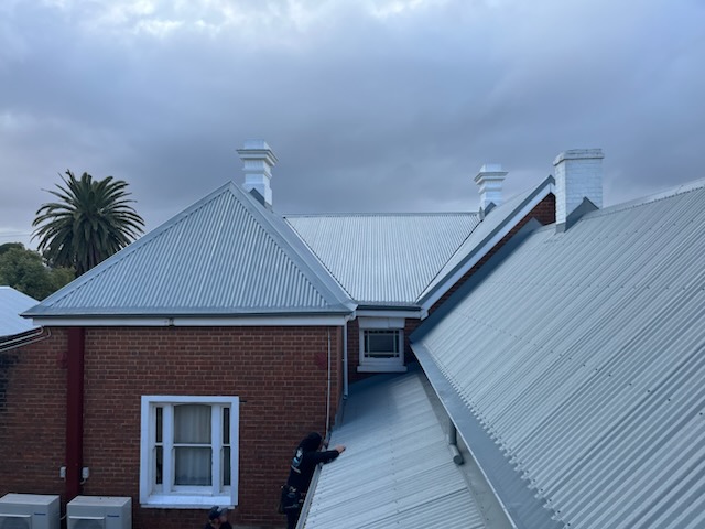 A Breens roofer working on a heritage re-roof, new pale grey Colorbond and white chimneys